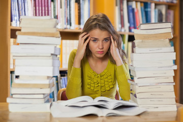 Tired pretty student studying between piles of books