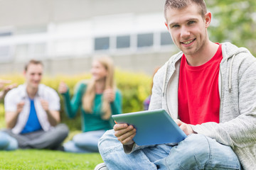 Fototapeta na wymiar Smiling college boy holding tablet PC with students in park