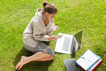 Student using mobile phone laptop with books at the park