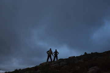 Couple with hands on hips on rocky landscape against sky at nigh