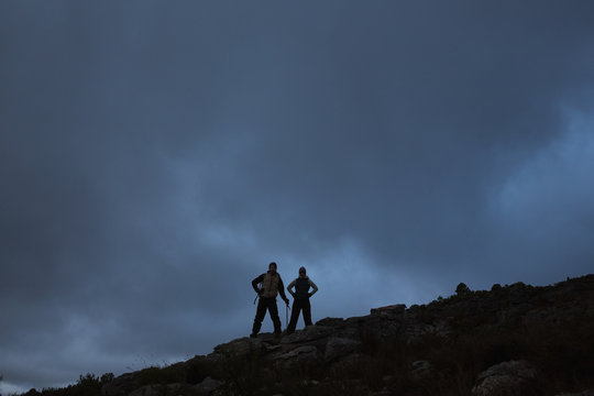 Couple with hands on hips on rocky landscape against sky at nigh