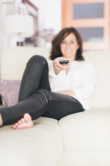 Woman using TV remote control while lounging on the sofa at home
