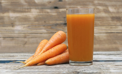 Carrot juice in glass with fresh organic carrots on white wooden