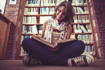 Happy female student against bookshelf reading a book on the lib