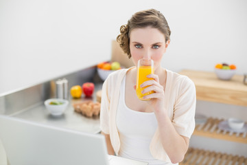 Fototapeta premium Cute woman drinking a glass of orange juice sitting in her kitch