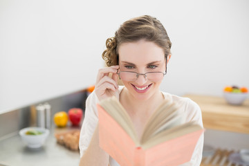 Cheerful woman reading a book while wearing glasses and sitting