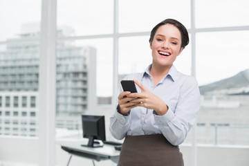 Cheerful businesswoman holding mobile phone in office