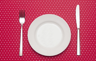 Empty white dinner plate with utensils on fun red polka dot tabl