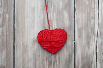 a heart made of red wool yarn hanging on old wood background.
