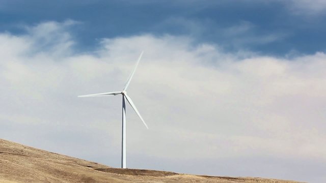 Single wind turbine turning on hillside with blue sky and clouds