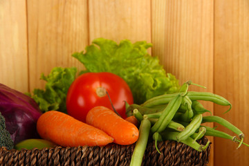 Different vegetables in basket on wooden background
