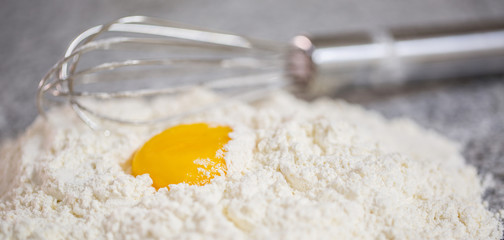 Flour, egg yolk and egg beater on a granite counter surface.