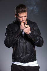 young man in leather jacket is lighting his cigar