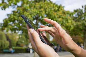 Woman using her cell phone in a park, trees background
