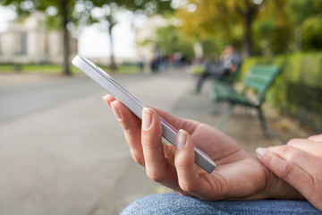 Woman with a cell phone, in a park on a bench, reading a message