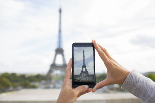Woman taking pictures in front of Eiffel Tower, cell phone
