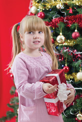 Pretty little girl smiling with present near the Christmas tree
