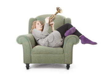 young pretty woman playing the trumpet in an armchair