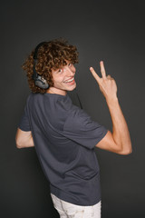 Happy male in headphones gesturing V sign over shoulder