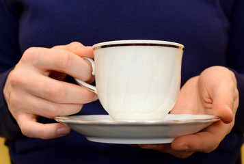 Closeup of a woman's hands holding a teacup and saucer