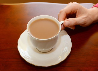 Woman picking up a cup of tea from a table