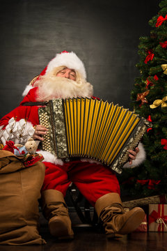 Santa Claus sitting in armchair near Christmas Tree at home and