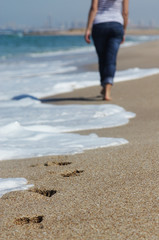 Young woman walking at the beach. Focus on the sand.