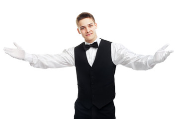 Young smiling waiter opens his arms in welcome