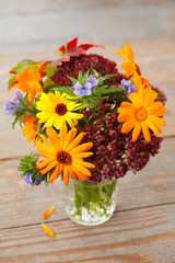 Bouquet of autumn flowers in vase on wooden background