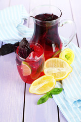 Red basil lemonade in jug and glass, on wooden background