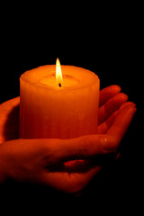 Burning candle in hands isolated on black