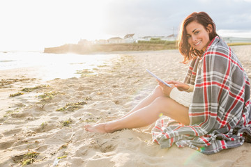 Woman covered with blanket using tablet PC at beach
