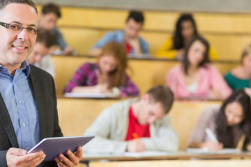Fototapeta na wymiar Teacher using tablet PC with students sitting at lecture hall