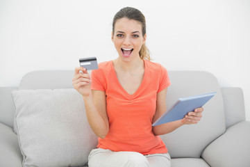 Cheering brunette woman showing her credit card holding her tabl