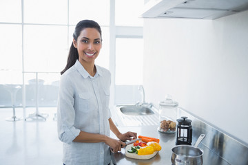Cute smiling woman preparing salad standing in bright kitchen
