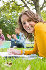 Female writing notes with students using laptop in park