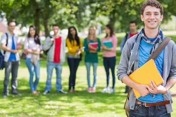 Obraz premium College boy holding books with students in park
