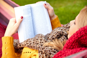 Young woman resting in a hammock and reading a book