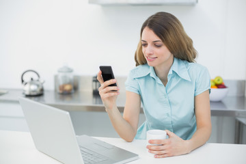 Content brunette woman making use of her smartphone holding a cu