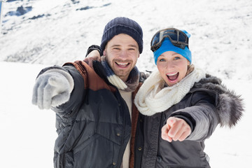 Fototapeta na wymiar Cheerful couple in jackets pointing at camera on snow covered la