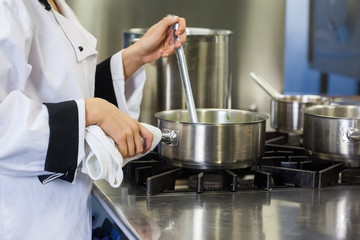 Young chef stirring with ladle holding pot