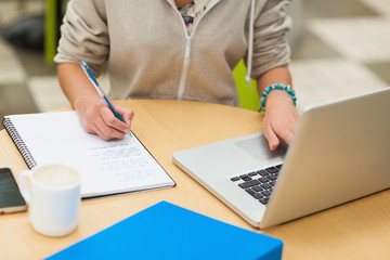 Mid section of a female student doing homework by laptop