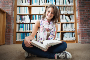 Happy female student against bookshelf with a book on the librar