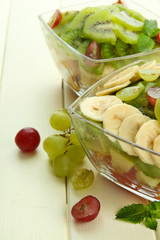 Tasty fruit salad in glass bowls, on white wooden table