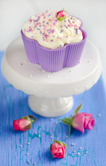 Vanilla cupcake with a rose on top of a blue wooden table