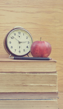 Vintage clock and apple with pancil on old books