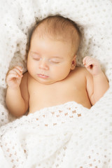 Baby newborn sleeping covered with white woolen blanket