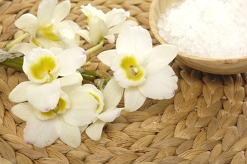Bowl of bath salt and branch orchid on woven wicker mat