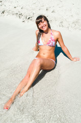 Fototapeta premium Joyful woman laying on white sand near sea water
