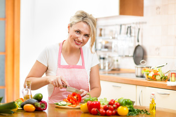 Cute woman cuts paprika for salad sitting at the kitchen table